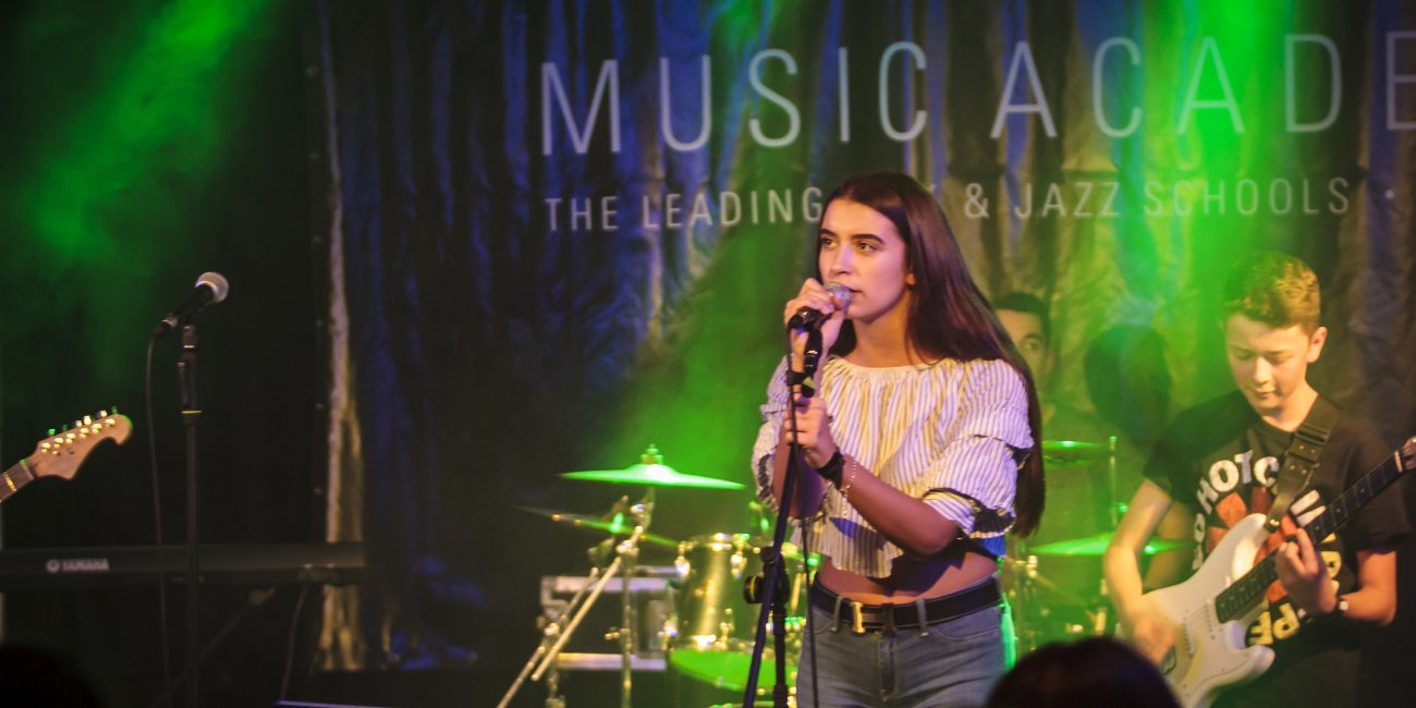 Schülerin singt auf der Bühne mit ihrer Band der Music Academy